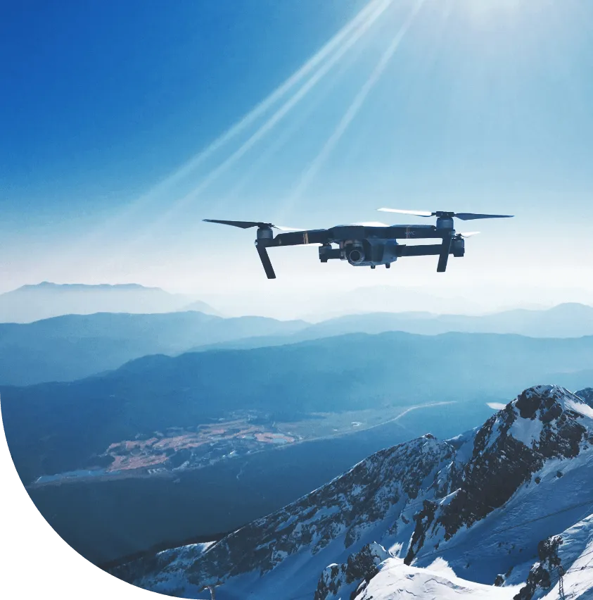 Quadcopter drone hovering above a snow-capped mountain range