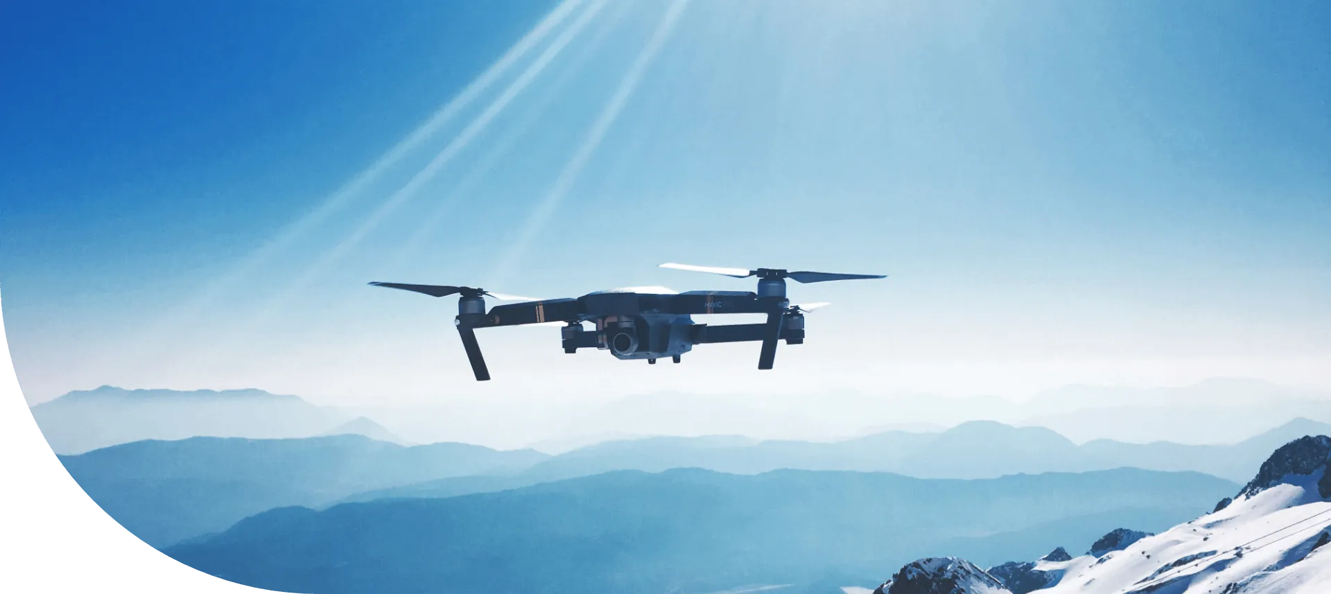 Quadcopter drone hovering above a snow-capped mountain range
