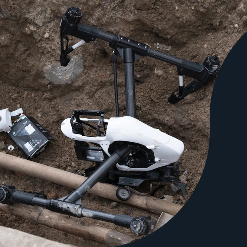 Crashed white drone lying across pipes on bare ground