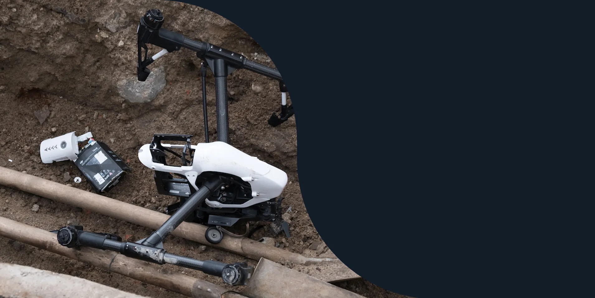 Crashed white drone lying across pipes on bare ground