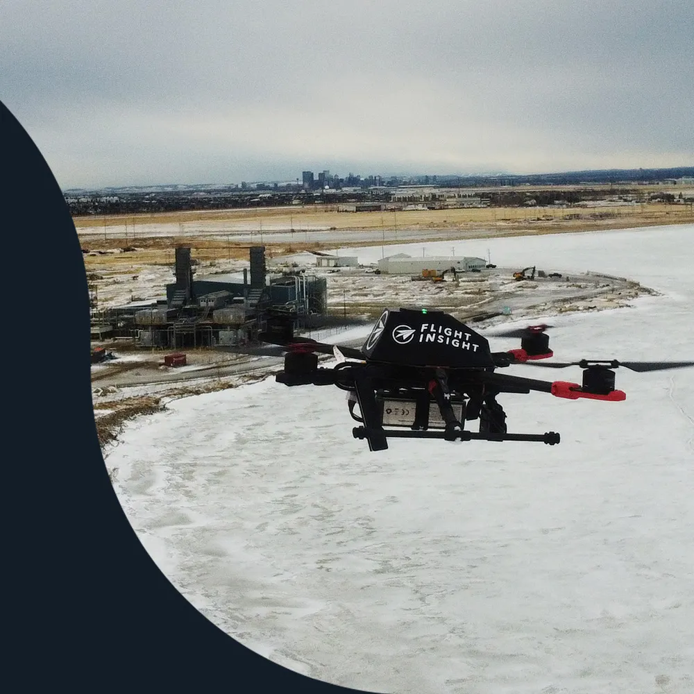 Quadcopter drone in flight over a frozen lake beside an industrial site
