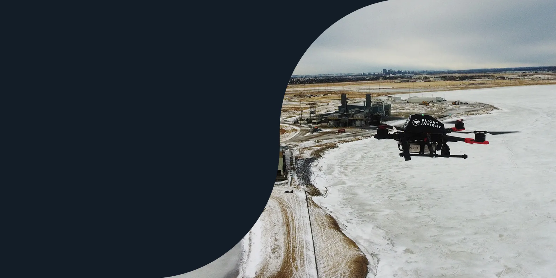 Quadcopter drone in flight over a frozen lake beside an industrial site